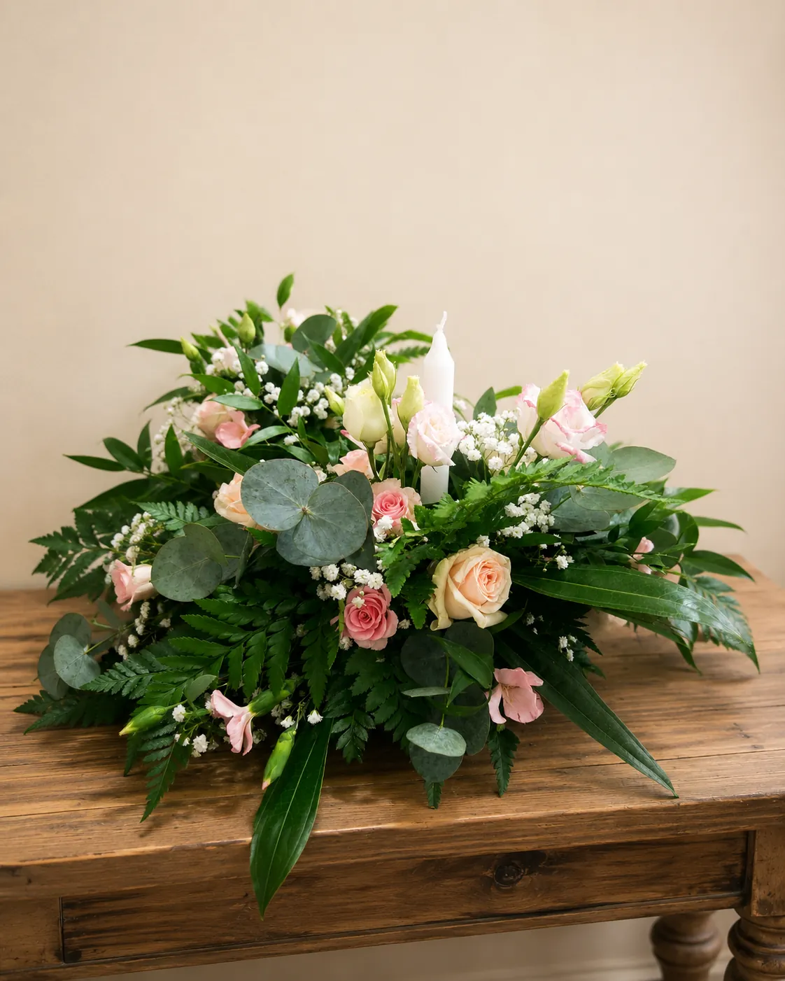 Soft pastel funeral tribute with peach roses and a memorial candle