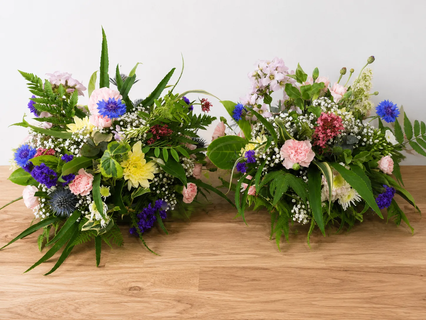 Pair of matching pastel funeral posy tributes with cornflowers and carnations