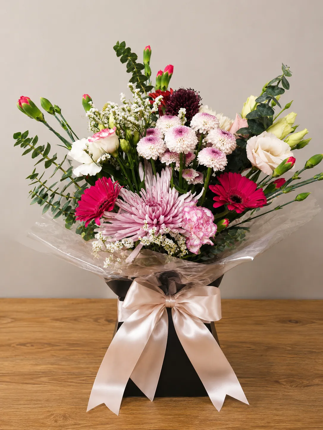 Pink and cream box arrangement with hot pink gerbera, chrysanthemum and lisianthus tied with a champagne ribbon