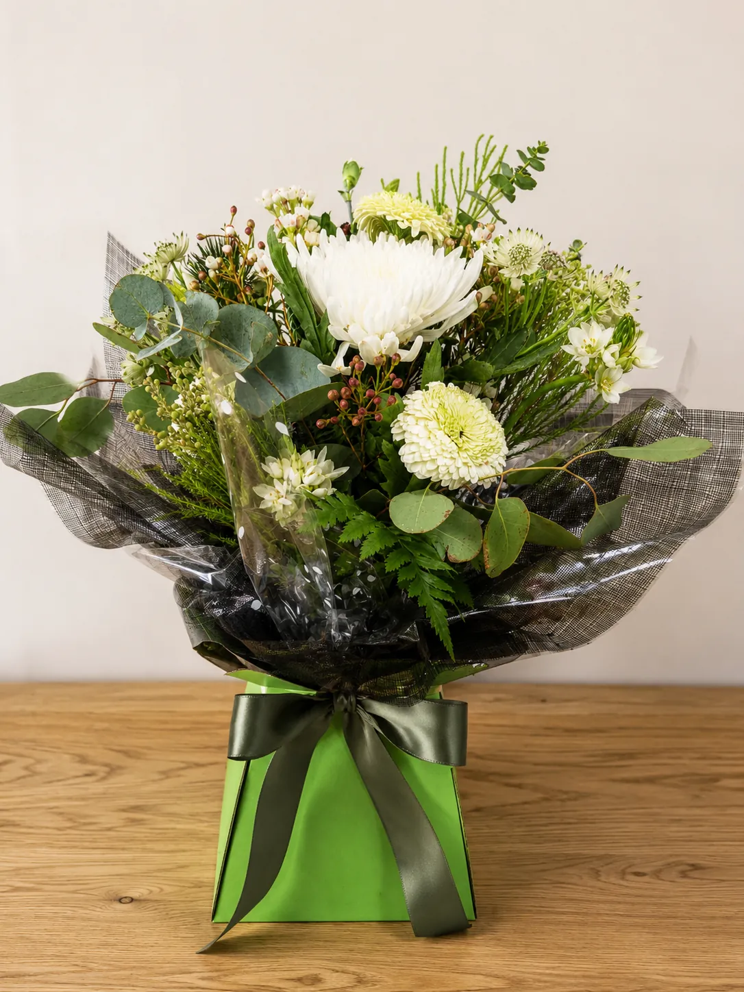 White chrysanthemum and eucalyptus box arrangement wrapped in black patterned foil with a sage green ribbon bow
