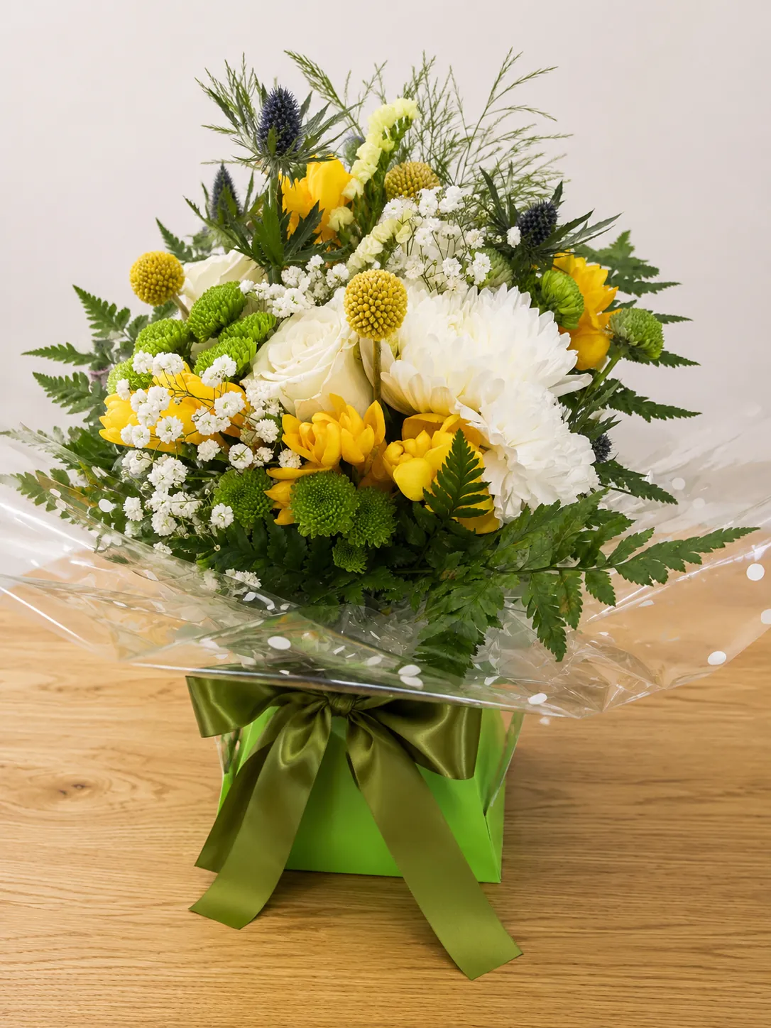 Yellow and white box arrangement with roses, craspedia and blue thistle in a green gift box