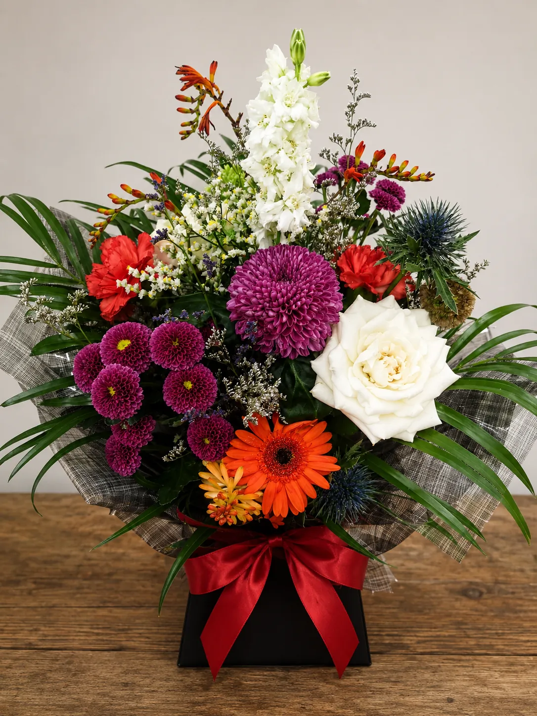 Vibrant box arrangement with purple chrysanthemum, red carnations and a white rose in a black gift box