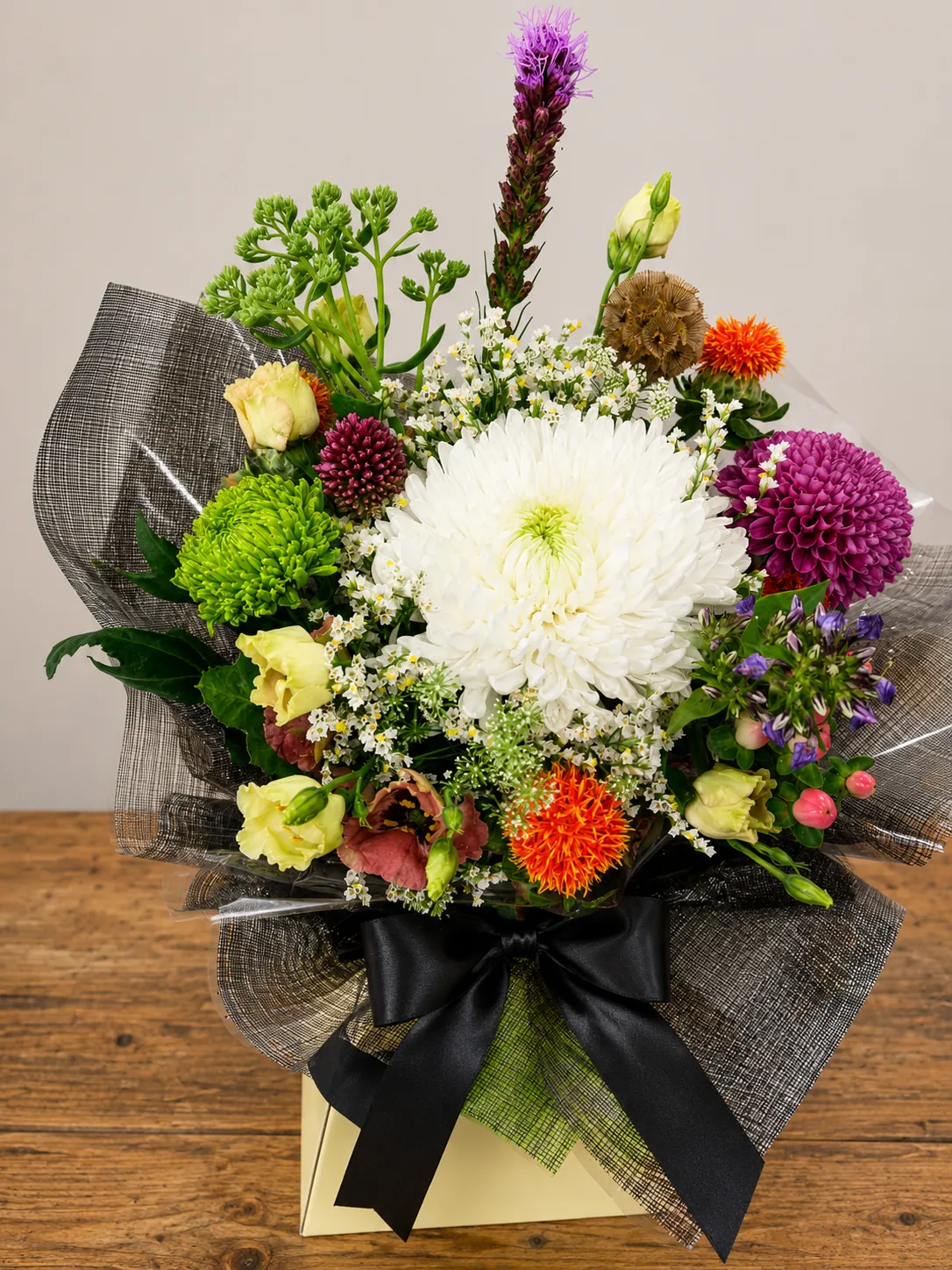 Colourful box arrangement with white chrysanthemum, purple dahlias and orange safflower in a monochrome wrap