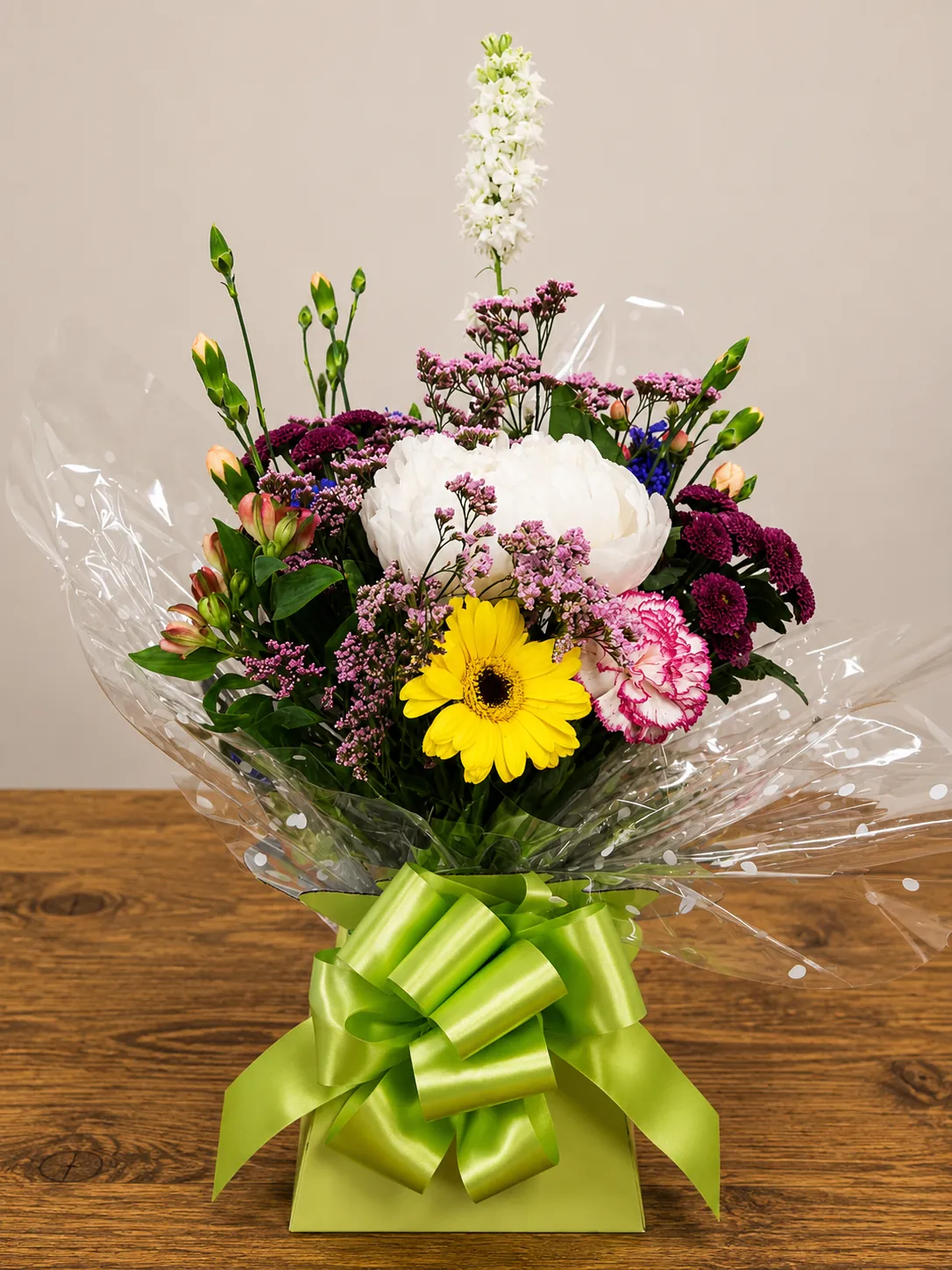 Jewel-toned box arrangement with a yellow gerbera, pink peony and purple chrysanthemum tied with a lime ribbon