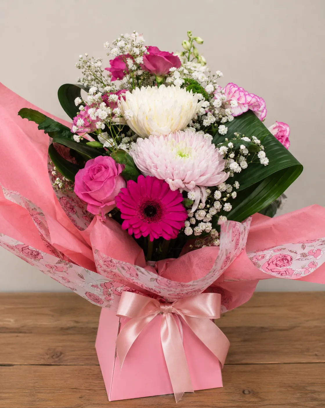 Pink box arrangement with fuchsia roses, gerbera and chrysanthemums wrapped in pink rose-print paper