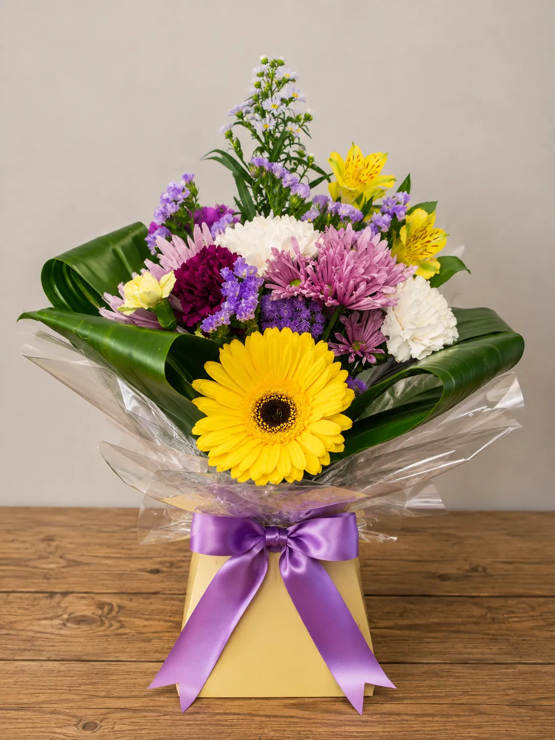 Bright box arrangement with yellow gerbera, purple carnation and alstroemeria in a yellow gift box with a purple bow