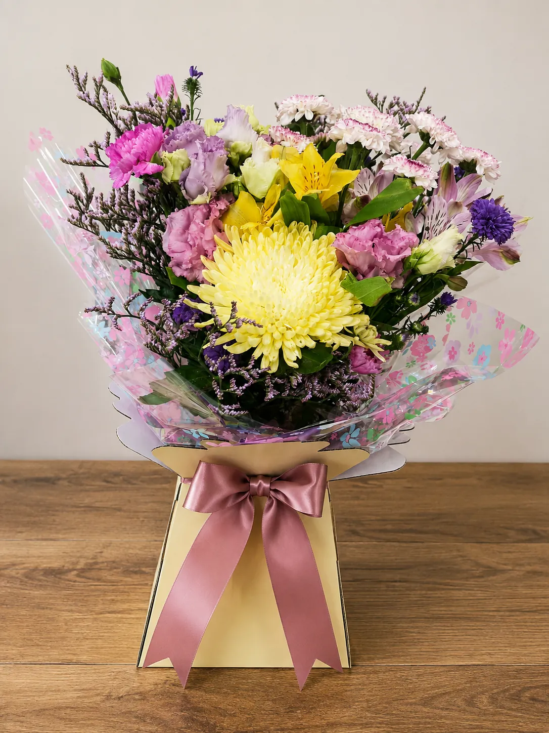 Pastel box arrangement with pink lisianthus, purple carnation and a yellow chrysanthemum in a floral wrap