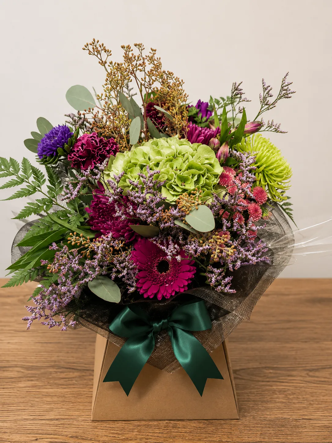 Jewel-toned box arrangement with green hydrangea, purple aster and a magenta gerbera wrapped in kraft paper