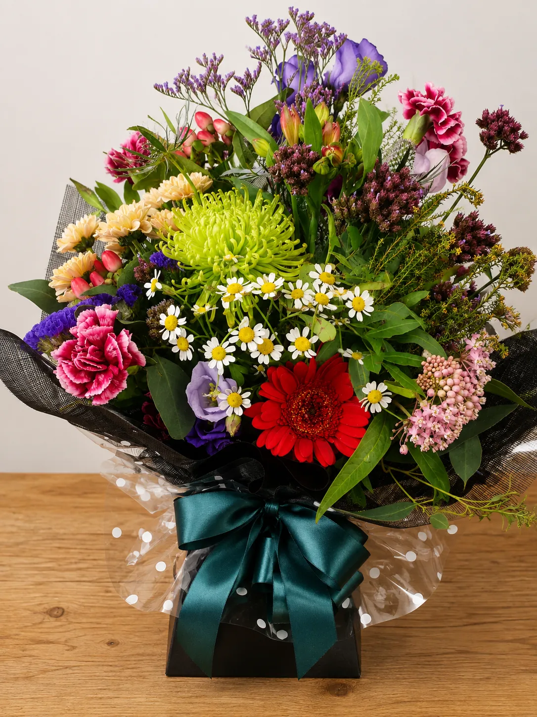 Jewel-toned box arrangement with green chrysanthemum, red gerbera and pink carnation wrapped in polka-dot cellophane