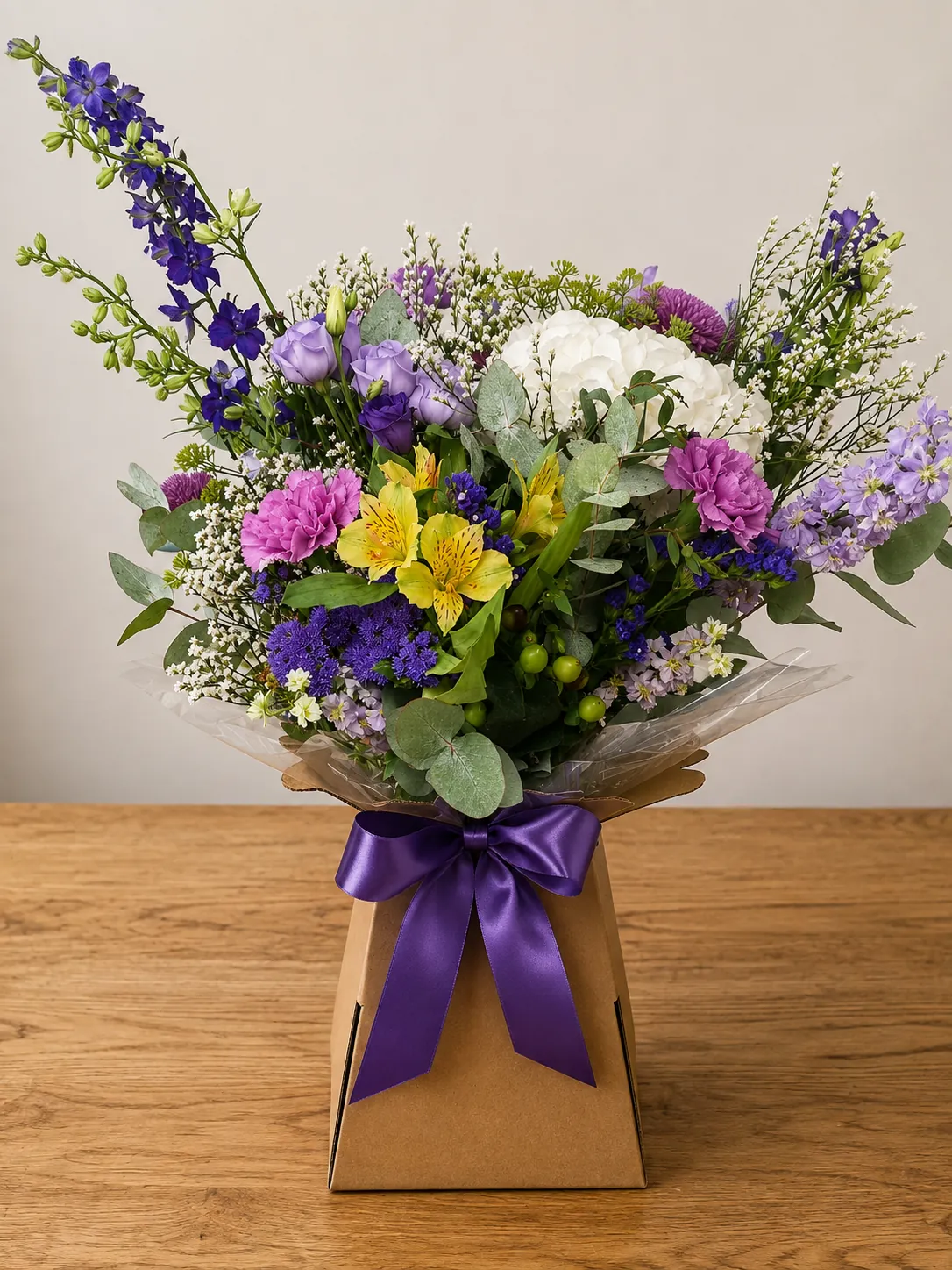 Purple and white box arrangement with delphinium, hydrangea and pink carnations in a kraft gift box