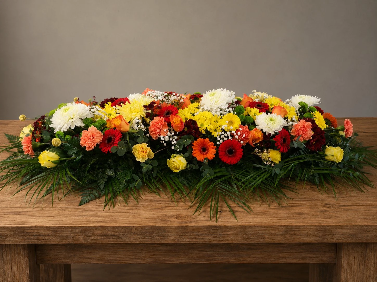 Colourful casket spray with orange, yellow and red flowers by Quality Plants and Flowers, Denby Dale