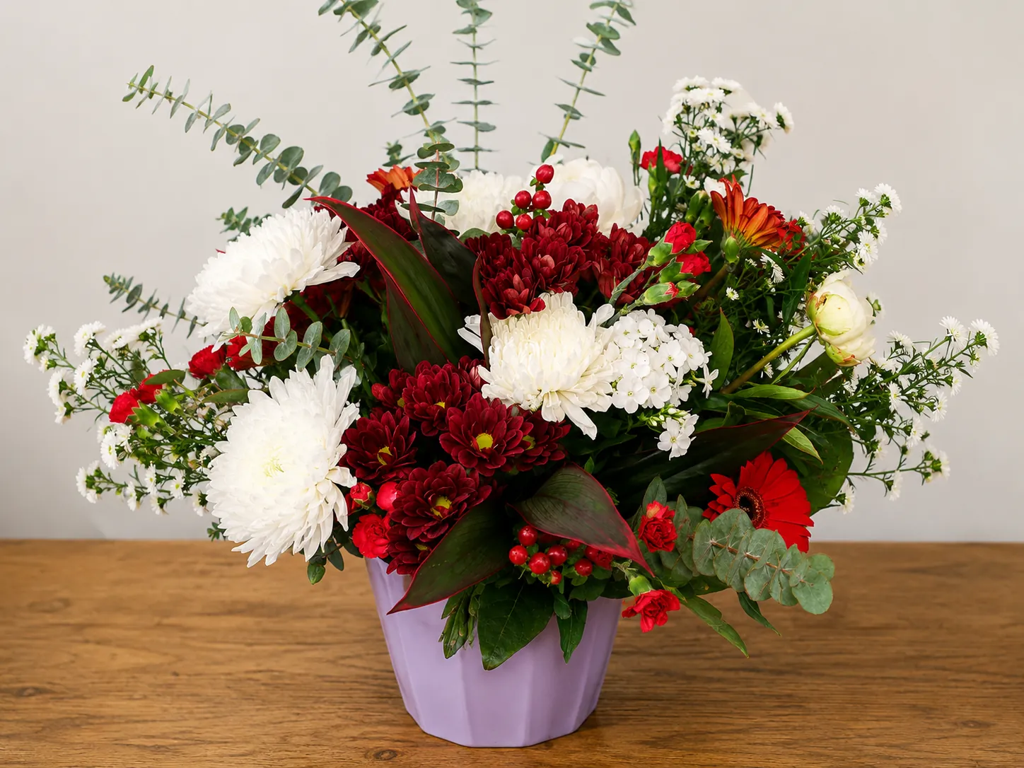Red and white flower arrangement in a lilac ceramic pot