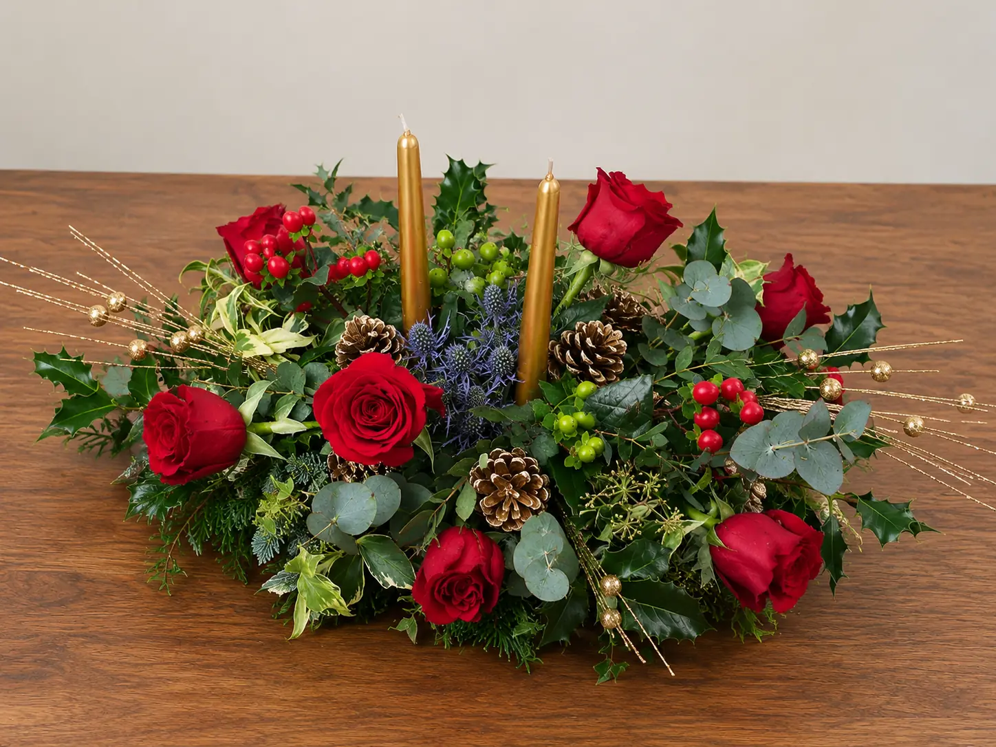 Christmas table centrepiece with candles, red flowers and foliage