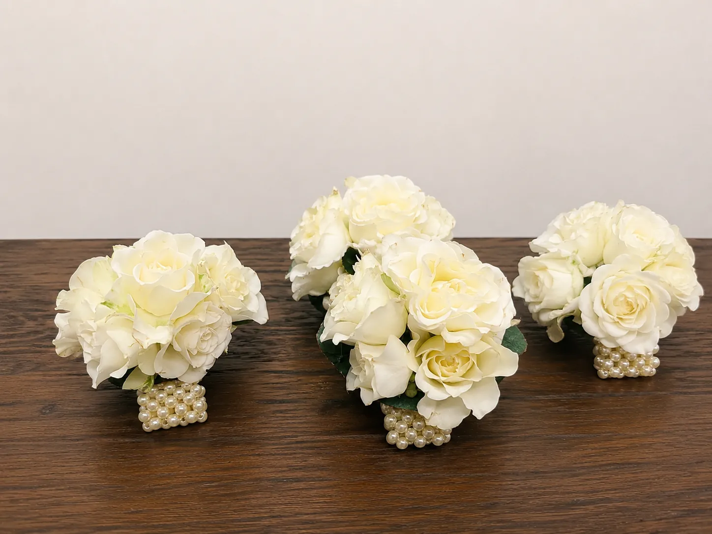 Trio of ivory rose wrist corsages with pearl bands for bridesmaids